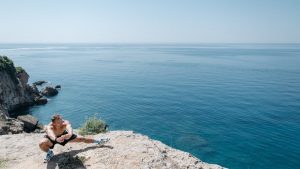 Shirtless man stretching on a cliff's edge by the ocean showcasing a healthy lifestyle and fitness.
